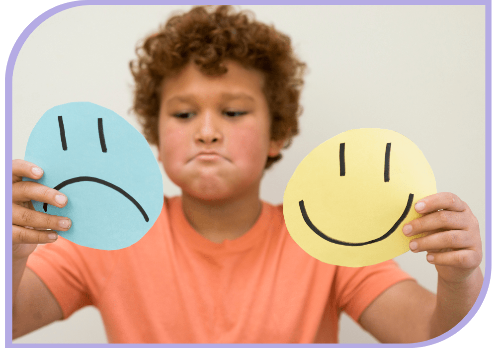 child facing camera eyes looking down at two round card he is holding, he has a sad face. The child is holding up two round cards with sad faces on them. Occupational Therapy - Able kids Therapy North Lakes