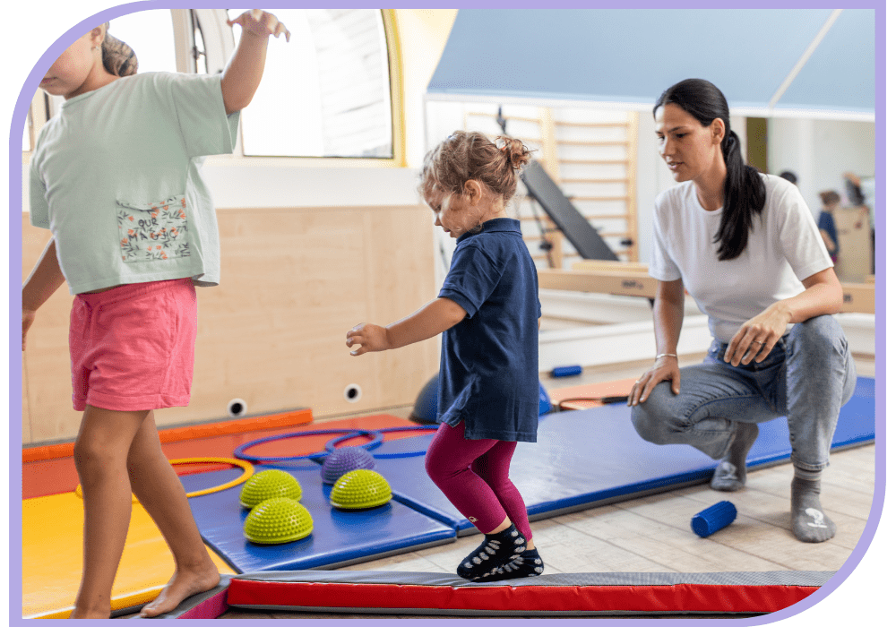 A therapist is watching/supporting two young children walk across a soft balance beam. Occupational Therapy - Able Kids Therapy