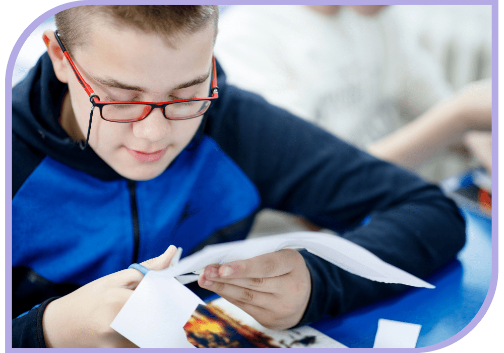 A child with glasses sits at a table while they carefully cut paper using scissors. Occupational Therapy - Able Kids Therapy