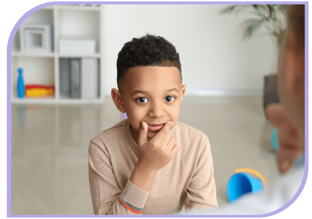 young boy is looking at the camera with his right thumb and index finger resting on either side of his mouth in the corner of his lips. Speech Therapy | Able Kids Therapy